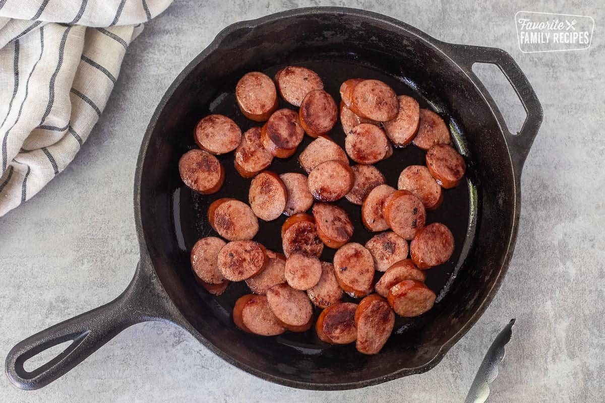 Skillet with sliced and browned smoked sausage to make creamy one pot tortellini