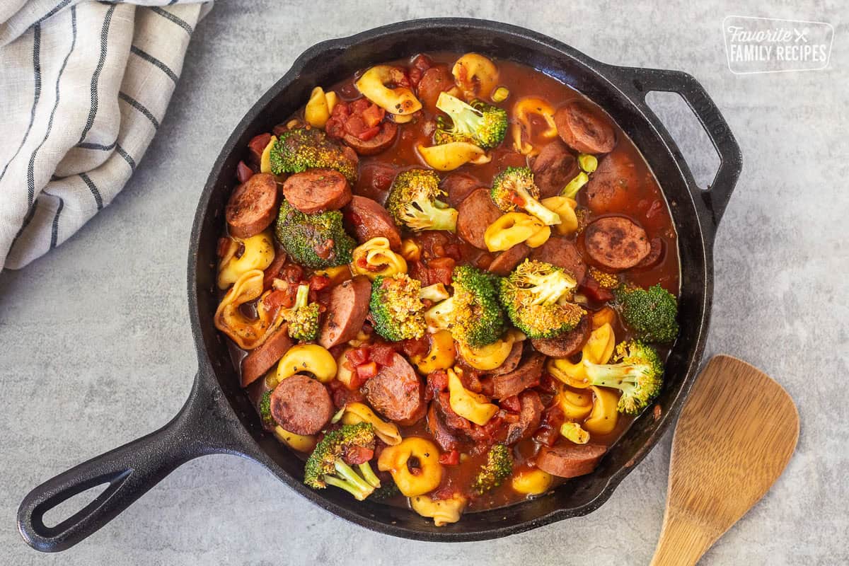 Skillet with cooked broccoli, tortellini and smoked sausage in a tomato sauce.