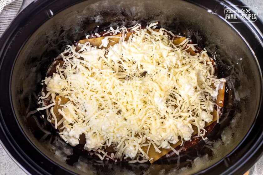 Crockpot with red sauce, noodles and cheeses.