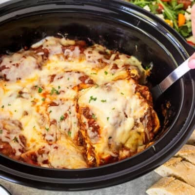 Lifting slice of crockpot lasagna with a spoon from the crockpot.