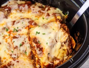 Lifting slice of crockpot lasagna with a spoon from the crockpot.