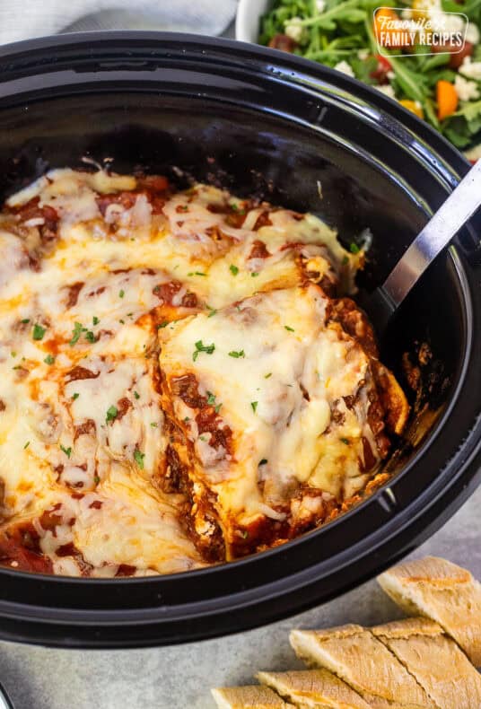 Lifting slice of crockpot lasagna with a spoon from the crockpot.