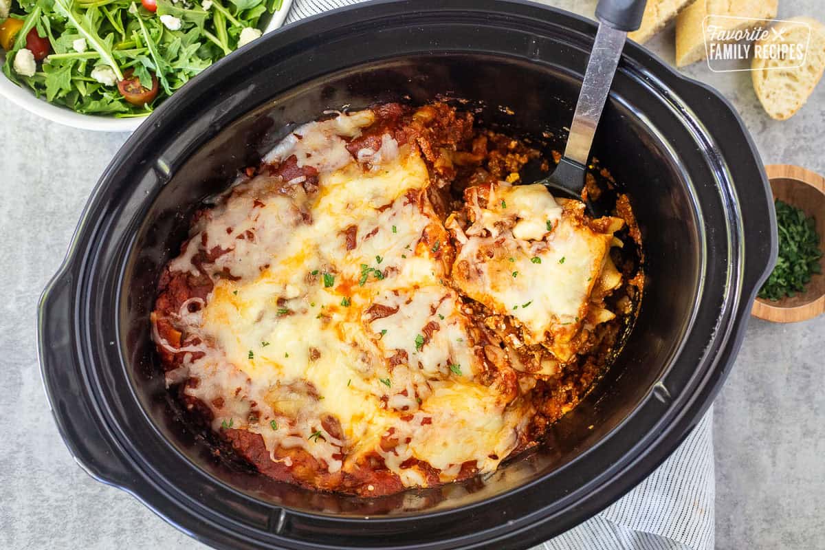 Lifting slice of crockpot lasagna with a spoon from the crockpot.