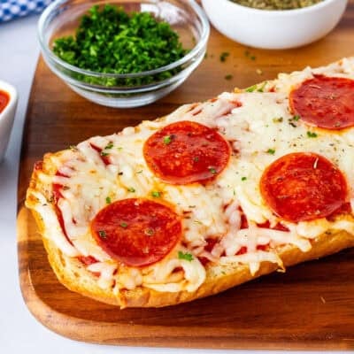 Half French bread pizza on a cutting board with dipping sauce on the side.