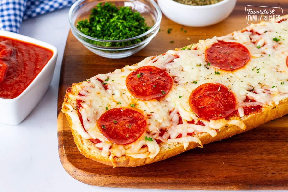 Half French bread pizza on a cutting board with dipping sauce on the side.