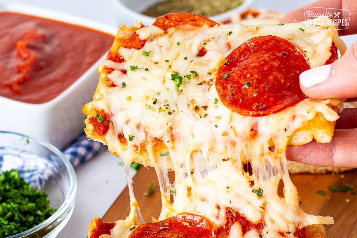 Hand picking up a slice of French bread pizza. 