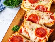 Cutting board with French bread pizza sliced.