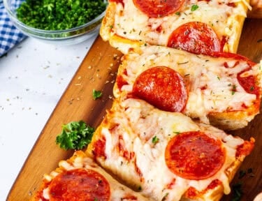 Cutting board with French bread pizza sliced.