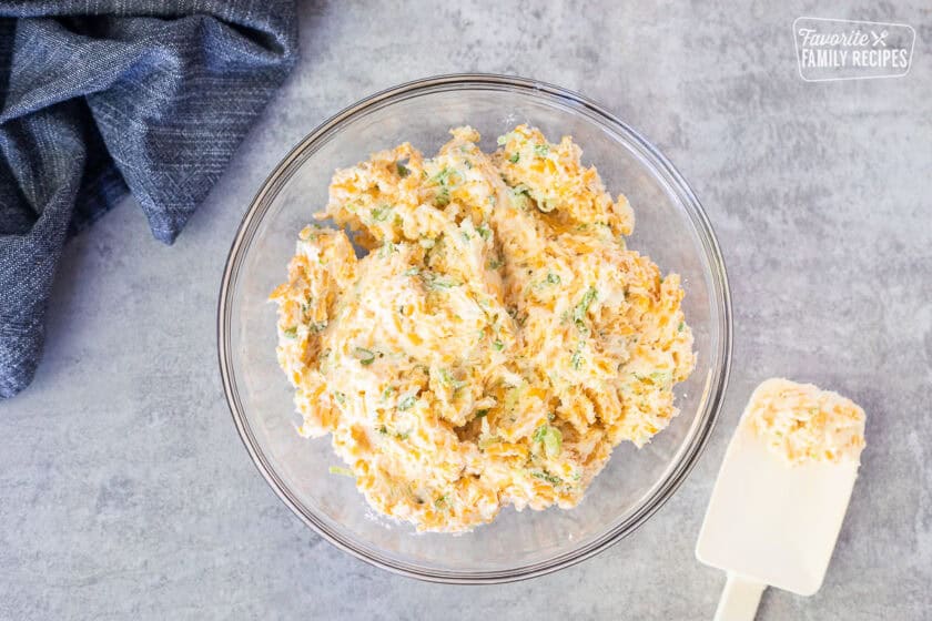 Glass mixing bowl with garlic cheese butter spread mixture. Spatula on the side.