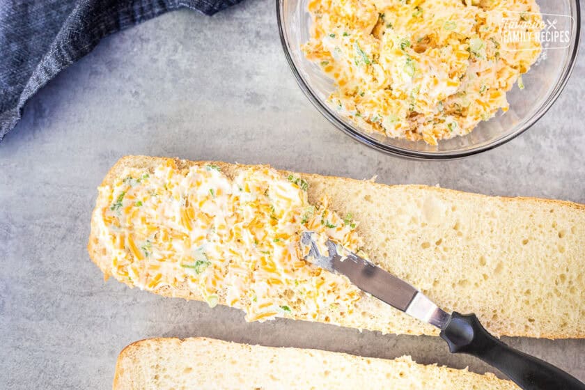 Spreading garlic bread with cheese mixture on cut French bread.