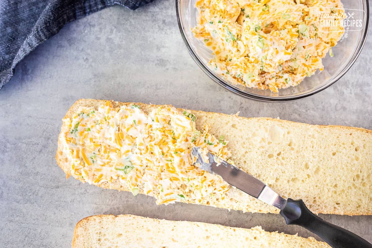 Spreading garlic spread mixture on cut French bread.