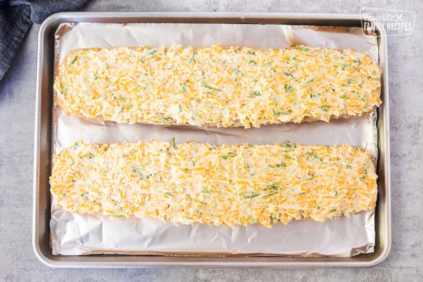 Foil lined sheet pan with two French bread loaf halves and covered with garlic bread spread.