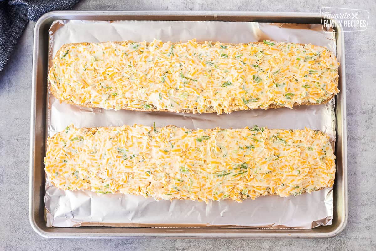 Foil lined sheet pan with two French bread loaf halves and covered with garlic bread spread.
