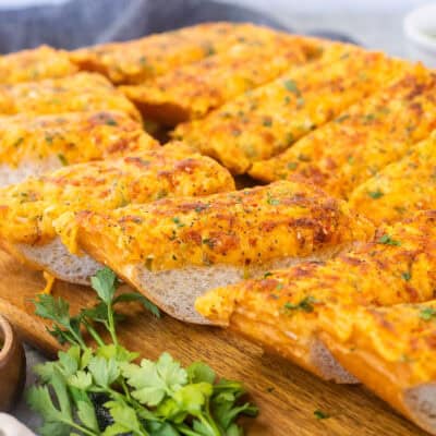 Sliced pieces of French bread baked with garlic bread spread on a cutting board.
