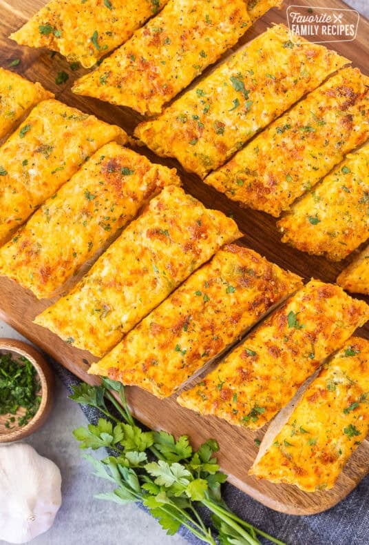 Sliced pieces of French bread with garlic bread spread on a cutting board.