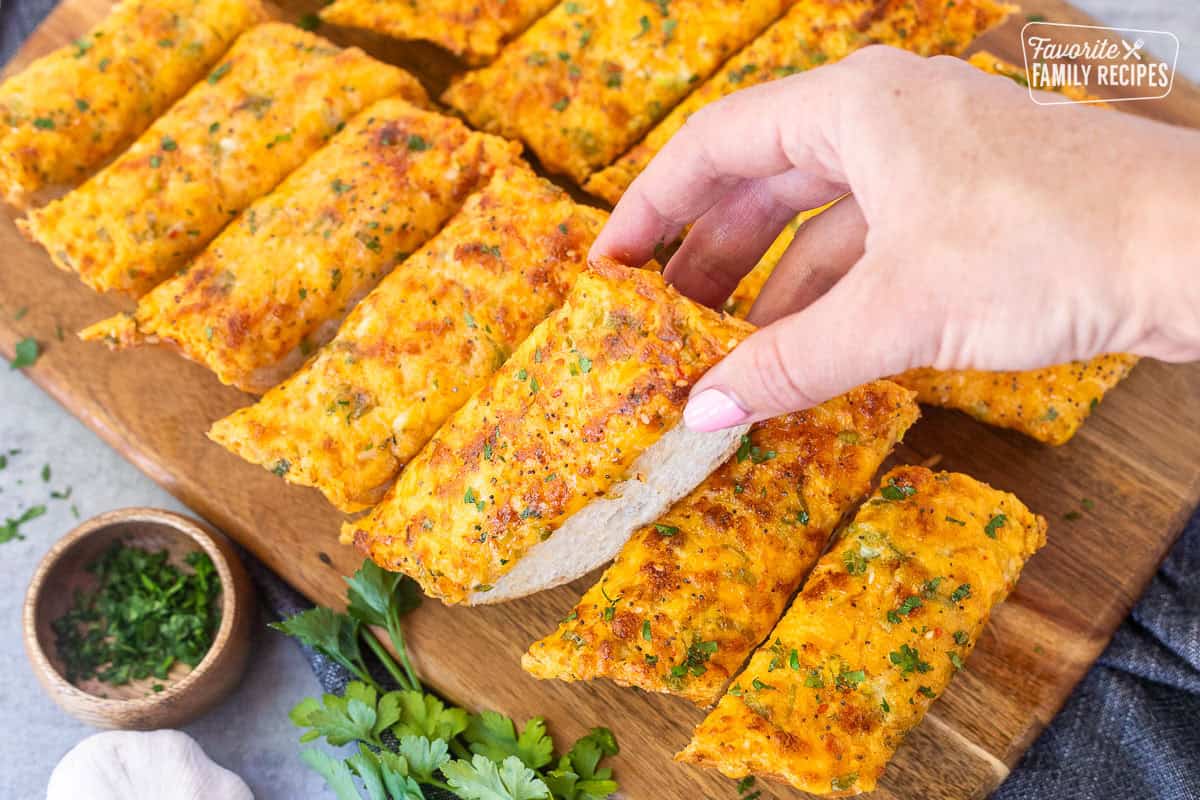 Hand picking up a piece of sliced French bread with garlic bread spread.