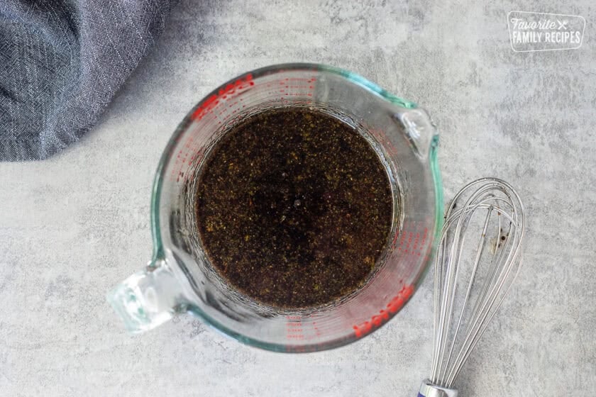 Glass container with mixed marinade and whisk on the side.