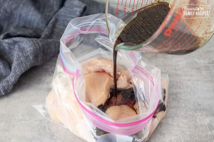 Pouring marinade on top of chicken breasts in a plastic bag.