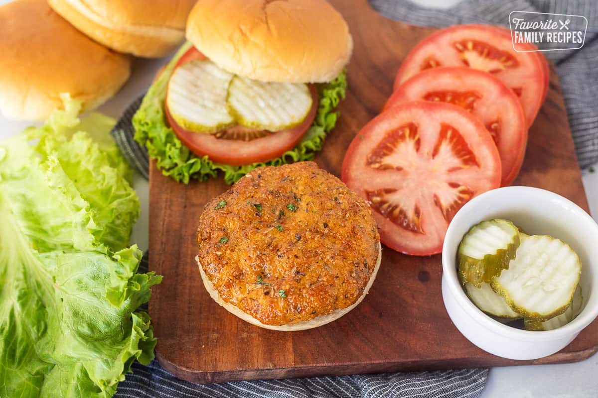 Placing a ground chicken patty on a bun with lettuce, tomato and pickles on the side.