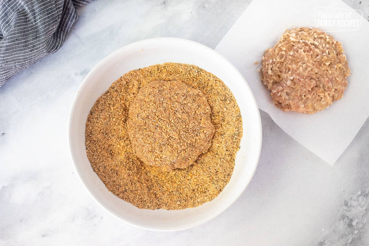 Shallow bowl with a chicken patty covered in a bread crumb mixture. Pressed chicken patty on the side.