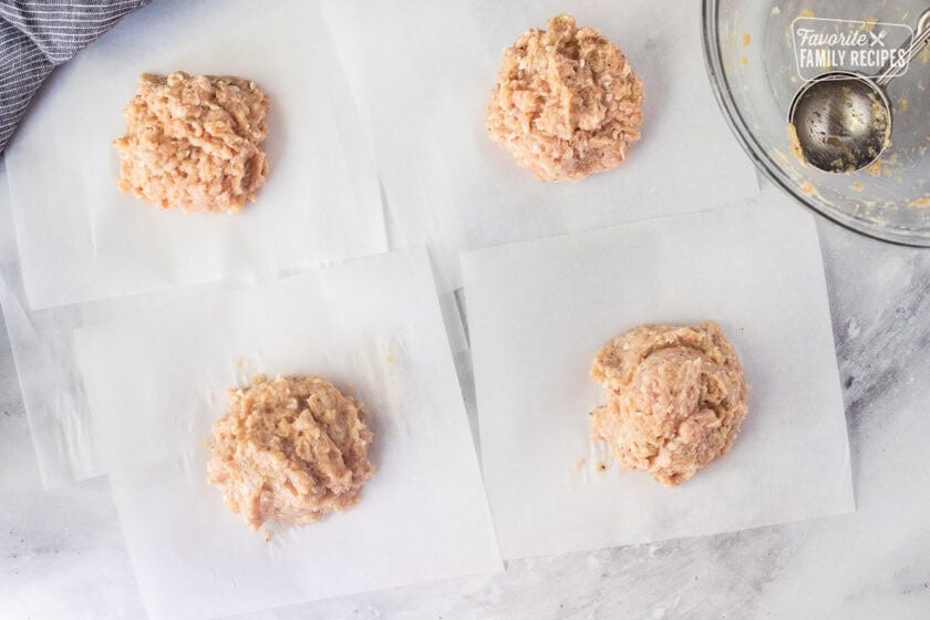 Four pieces of parchment paper with four portions of chicken mixture. Glass bowl with cookie scoop on the side.