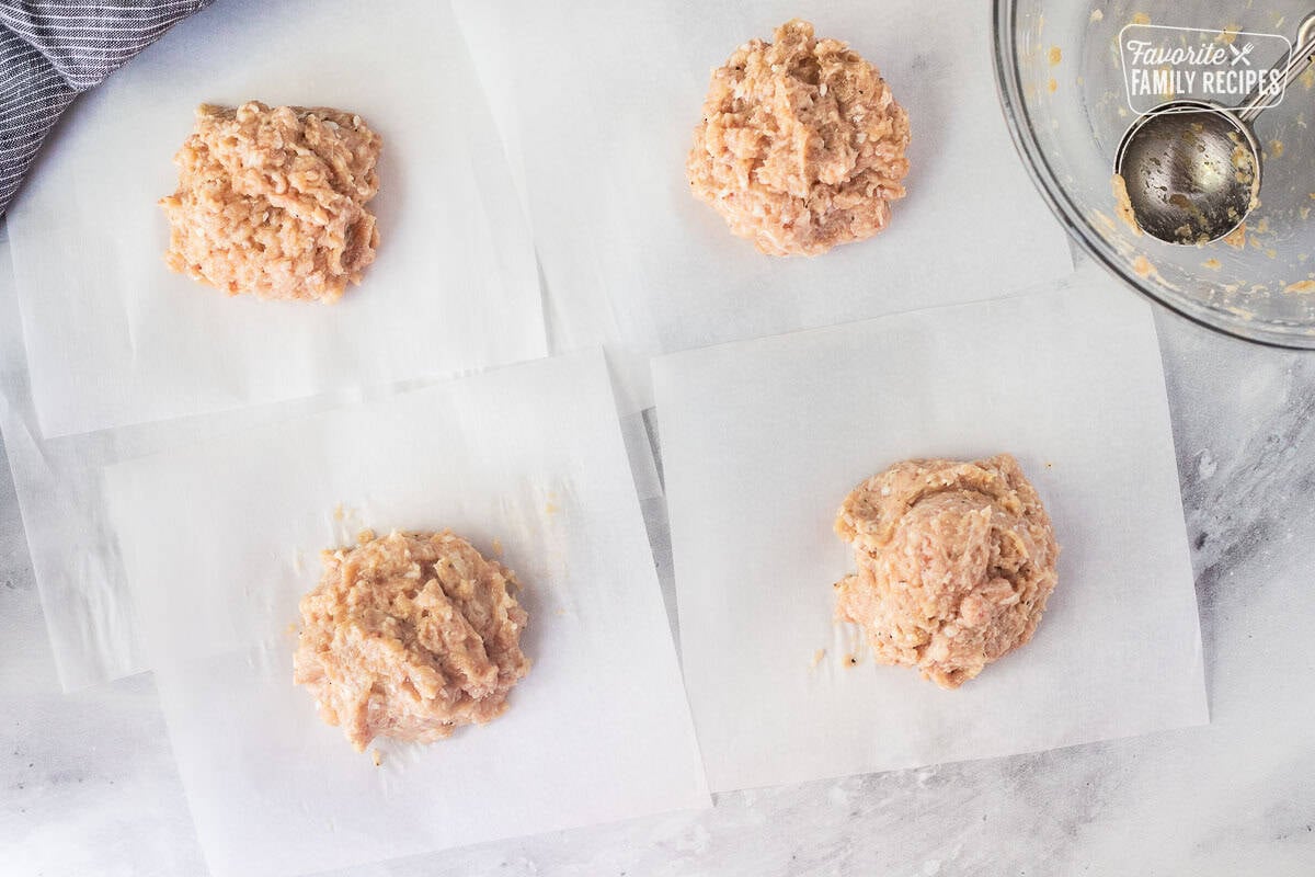 Four pieces of parchment paper with four portions of chicken mixture. Glass bowl with cookie scoop on the side.
