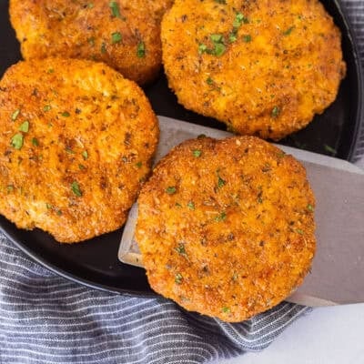 Spatula removing a ground chicken patty from a plate of ground chicken patties.