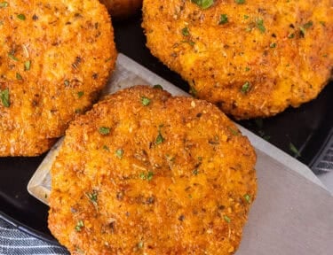 Spatula removing a ground chicken patty from a plate of ground chicken patties.