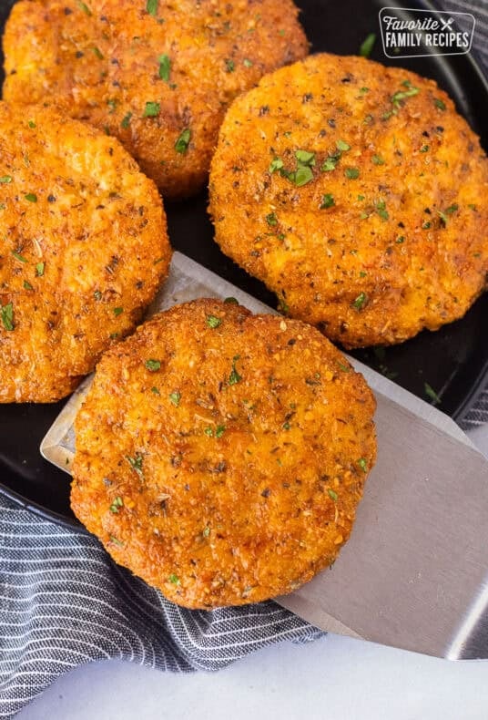 Spatula removing a ground chicken patty from a plate of ground chicken patties.