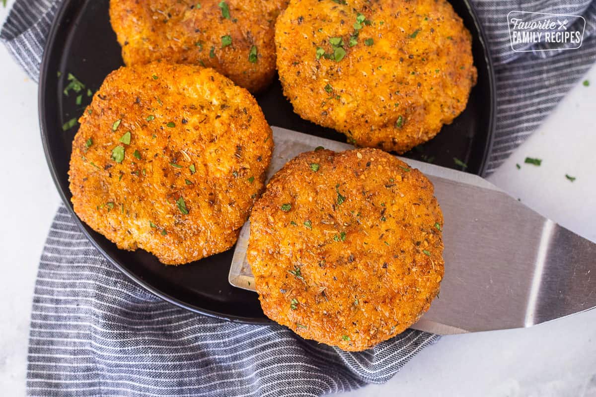 Spatula removing a ground chicken patty from a plate of ground chicken patties.