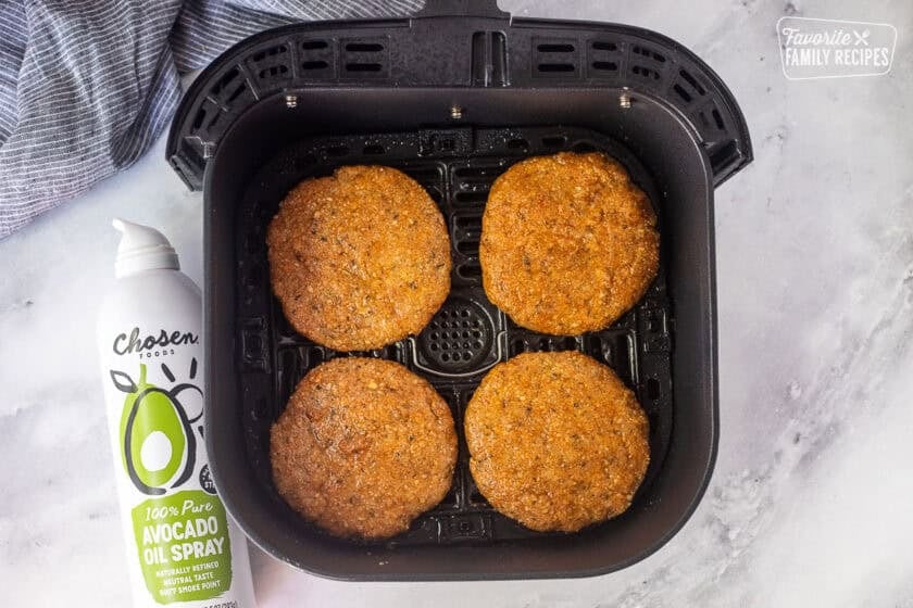 Four ground chicken patties in an air fryer tray sprayed generously with avocado oil spray.