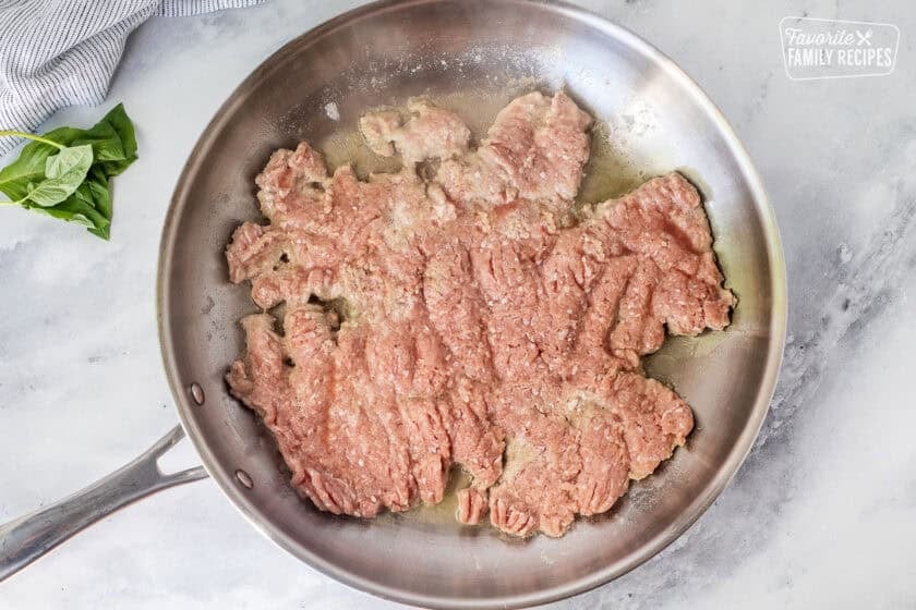 Skillet with ground turkey pressed flat in hot oil and butter.