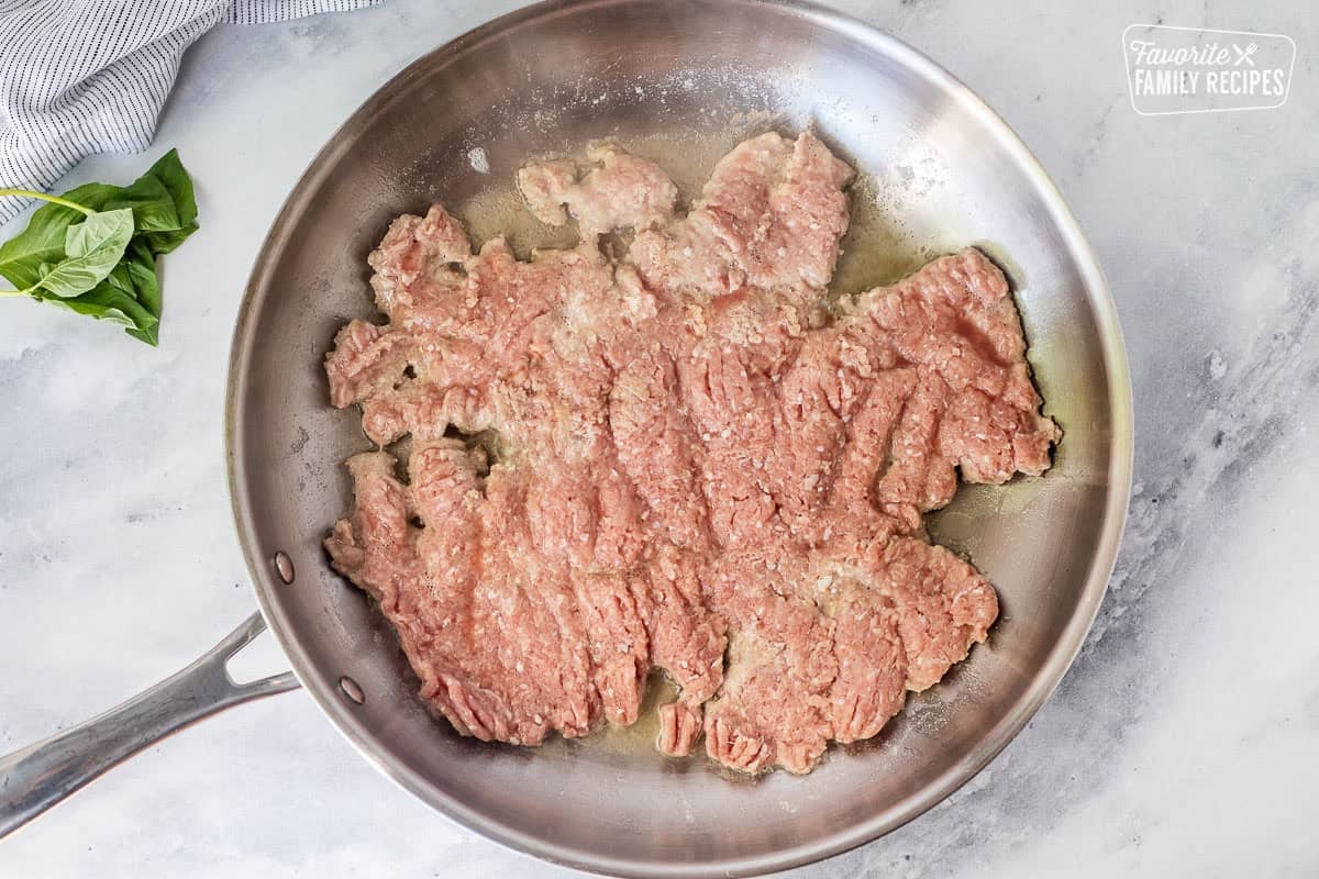 Skillet with ground turkey pressed flat in hot oil and butter.