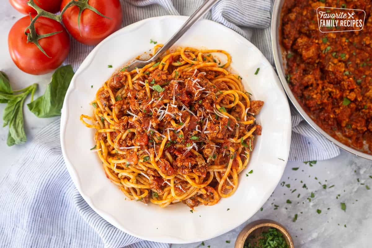 Shallow bowl with ground turkey spaghetti topped with fresh basil, parsley and fresh grated parmesan cheese.