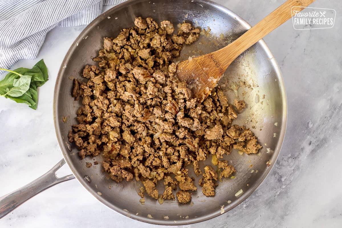 Skillet of ground turkey, onions and garlic with a wooden spoon.