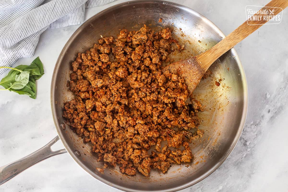 Skillet of ground turkey and tomato paste with a wooden spoon.
