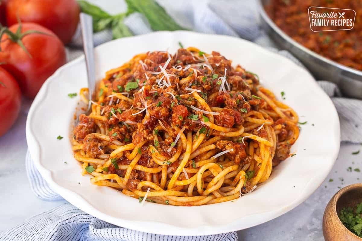 Glass plate of ground turkey spaghetti topped with fresh basil, parsley and fresh grated parmesan cheese.