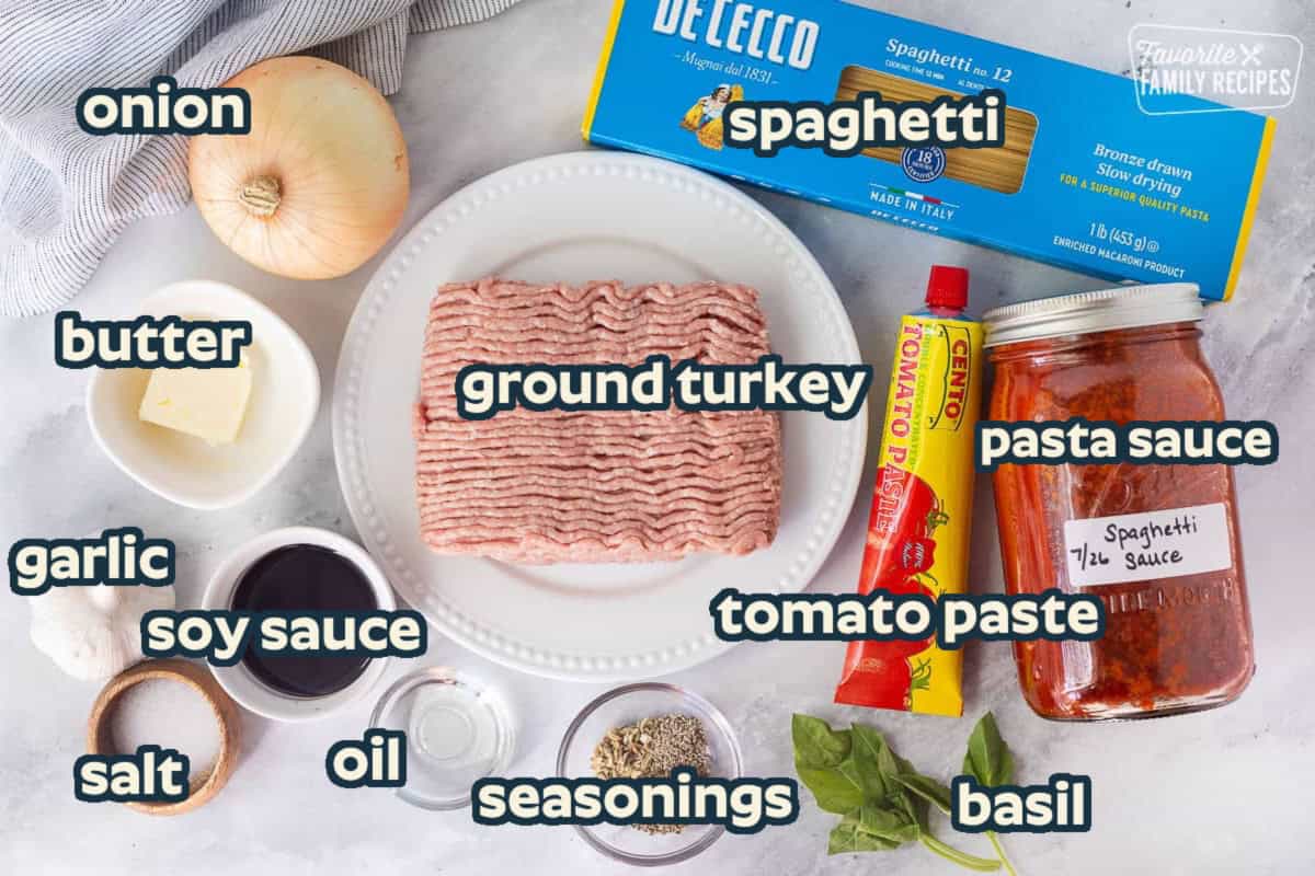 Ingredients to make ground turkey spaghetti including spaghetti noodles, homemade spaghetti sauce, tomato paste, ground turkey, onion, butter, soy sauce, salt, garlic, oil, oregano, pepper and fennel. Basil for garnish.