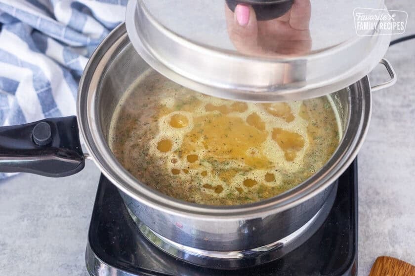 Placing lid on saucepan with boiling rice and seasonings over an electric skillet.