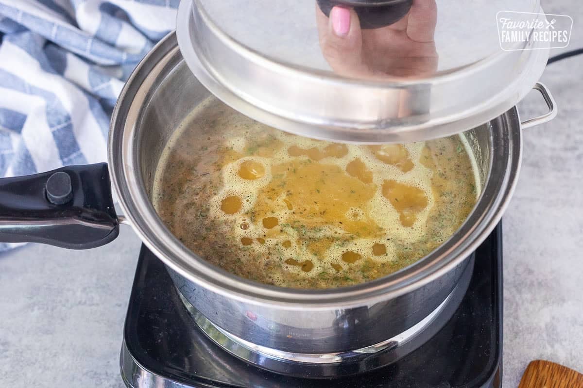 Placing lid on saucepan with boiling rice and seasonings over an electric skillet.
