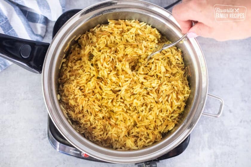 Fluffing up cooked homemade Rice-A-Roni with a fork in a saucepan.