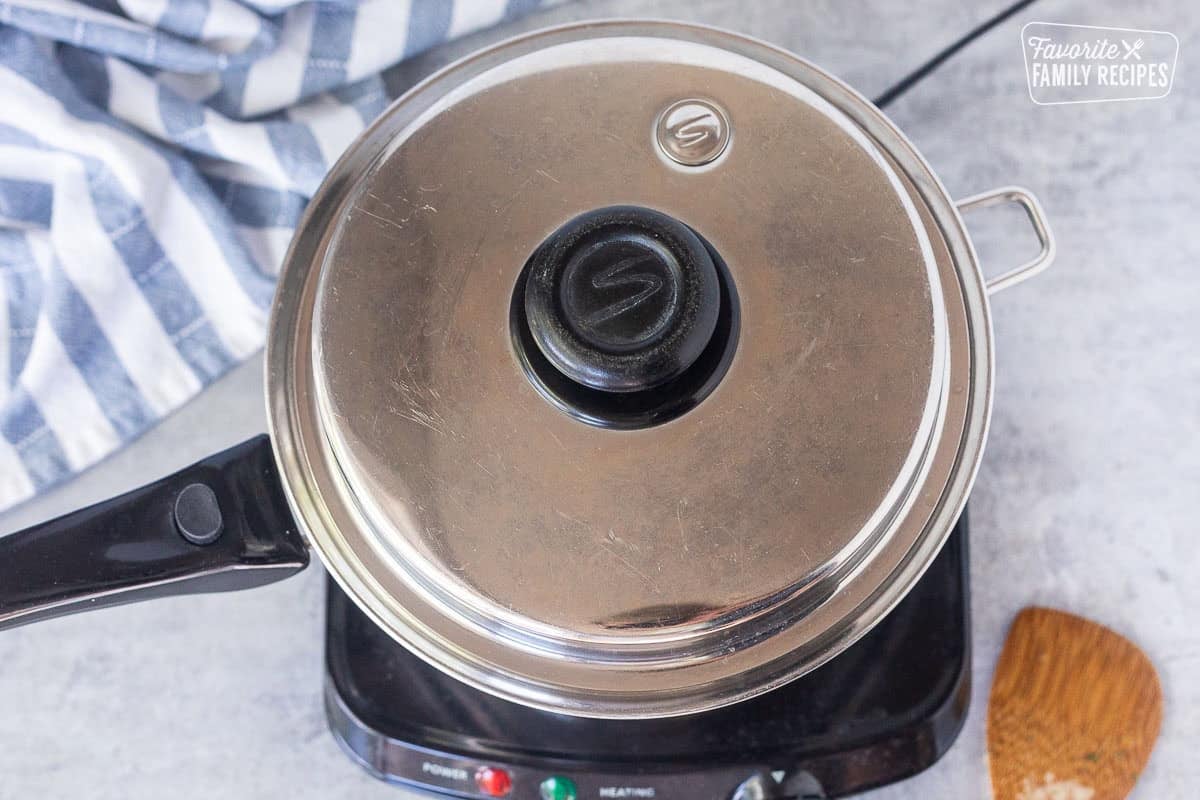 Lid on top of saucepan over electric skillet.