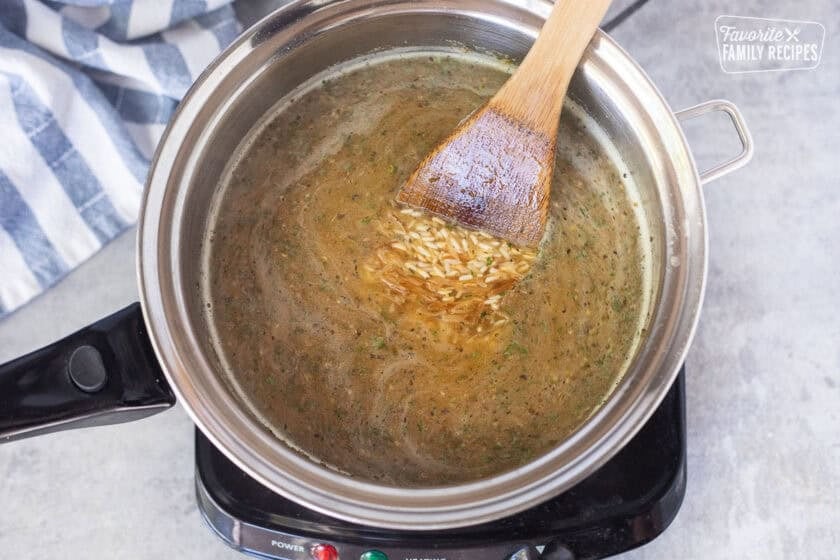 Stirring chicken broth with rice in a saucepan over electric skillet.