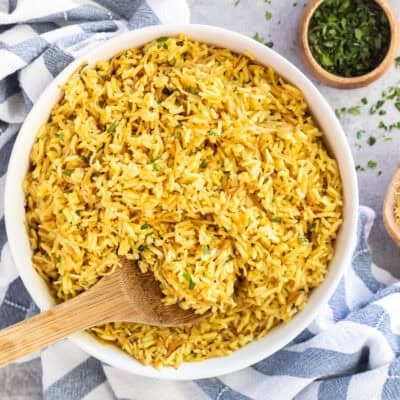 Glass bowl of homemade Rice-A-Roni garnished with parsley and wooden spoon.