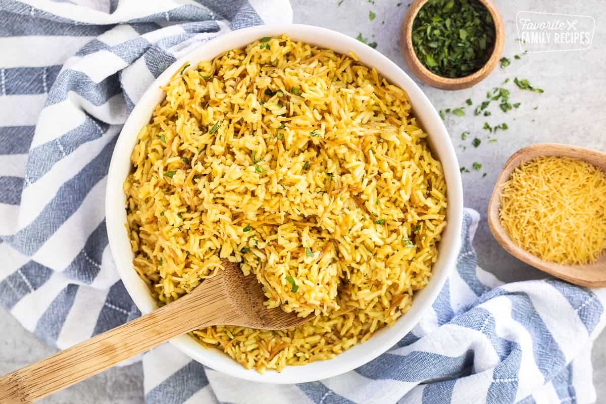 Glass bowl of homemade Rice-A-Roni garnished with parsley and wooden spoon.