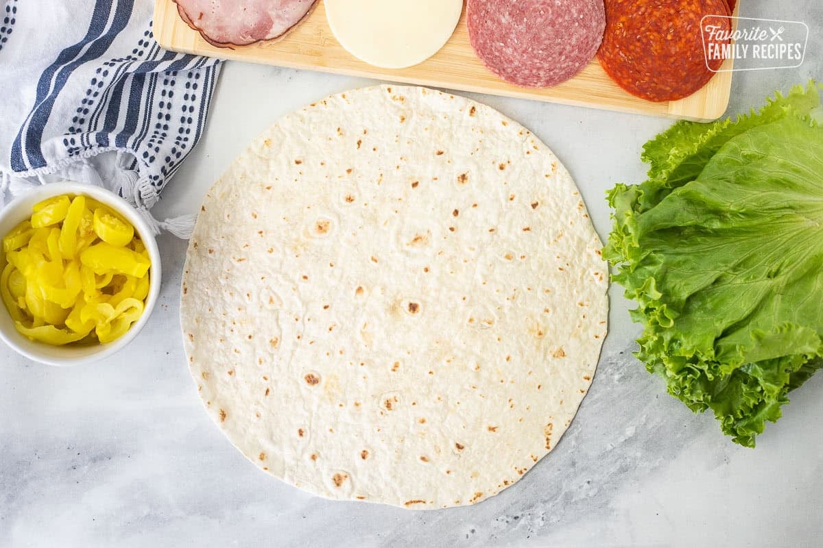 Tortilla with sides of lettuce, pepperoni, salami, provolone cheese, ham and banana peppers.