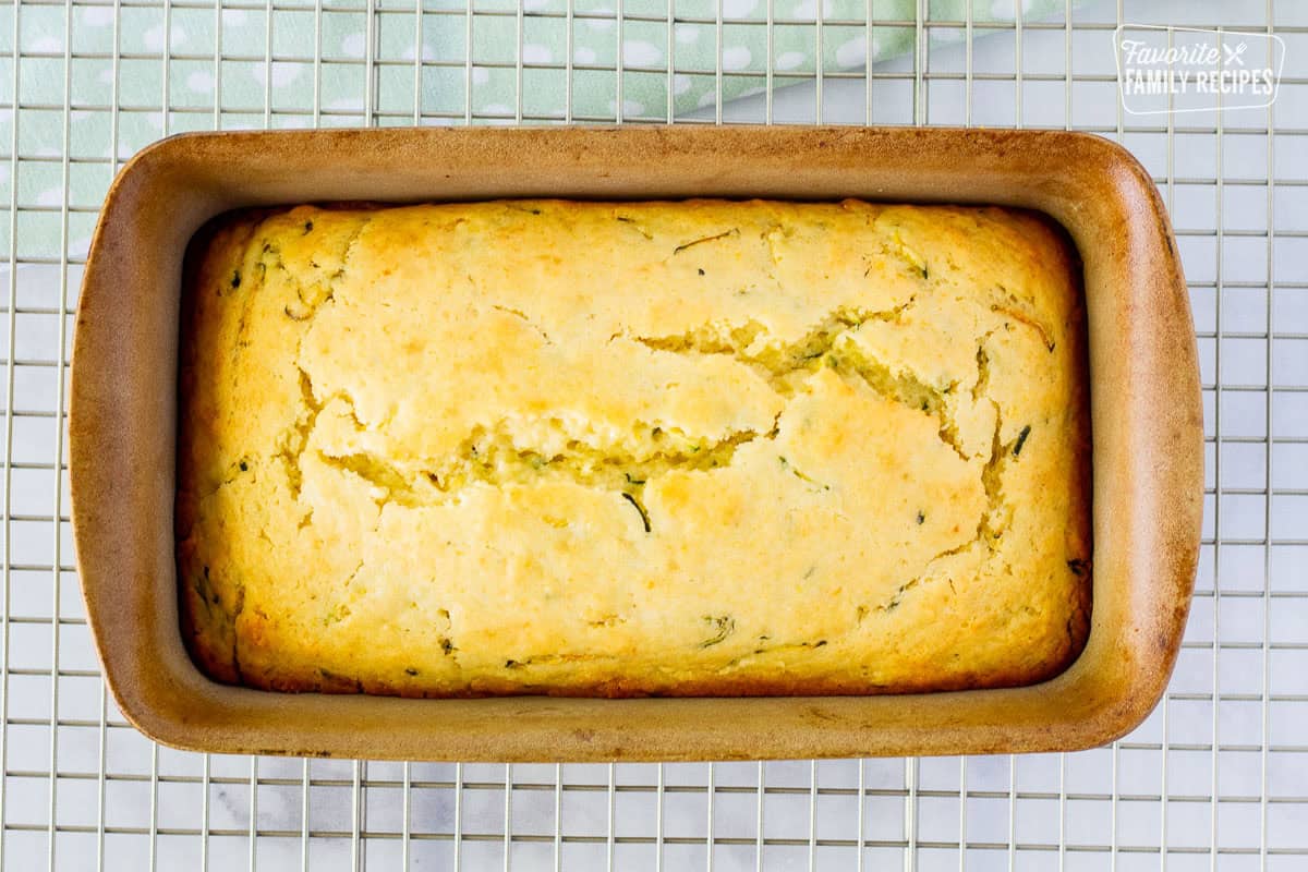 Baked lemon zucchini bread in a loaf pan resting on a cooling rack.
