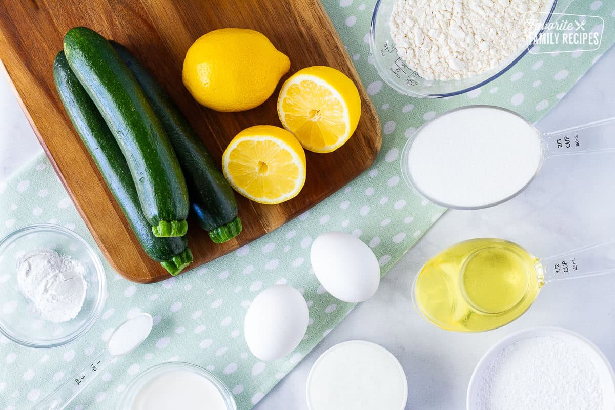 Ingredients to make lemon zucchini bread including flour, buttermilk, oil, eggs, powdered sugar, milk, sugar, zucchini, lemons, salt, baking powder and baking soda.