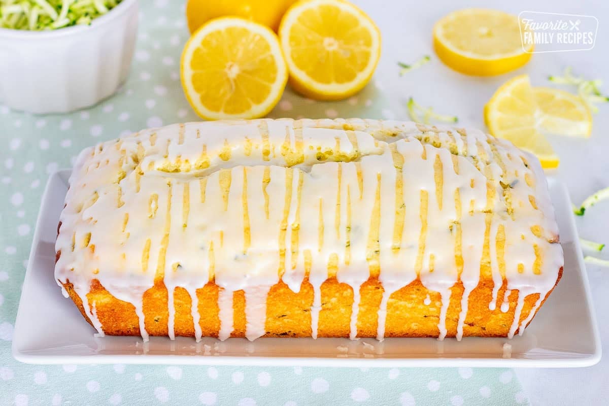 Whole glazed lemon zucchini bread loaf on a plate.