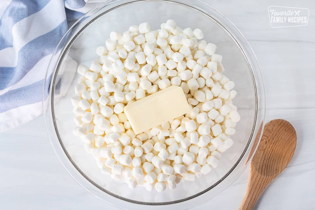 Glass mixing bowl with marshmallows and stick of butter. Wooden spoon on the side.